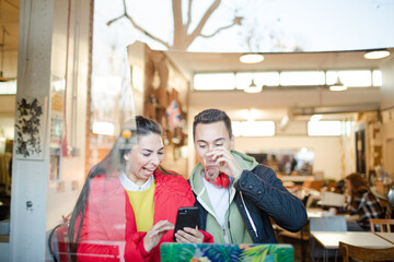 Young couple using smart phone and laptop in cafe