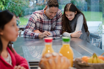 Smiling father and daughter using digital tablet at kitchen counter