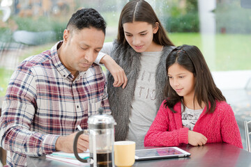 Father and daughters using digital tablet in morning kitchen
