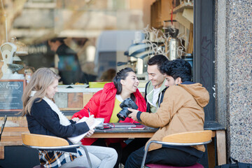 Young adult college students with digital camera at sidewalk cafe
