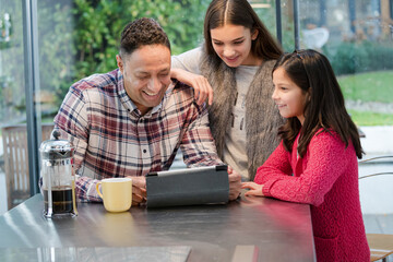 Father and daughters using digital tablet in morning kitchen