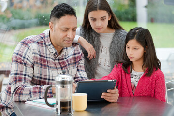 Father and daughters using digital tablet in morning kitchen