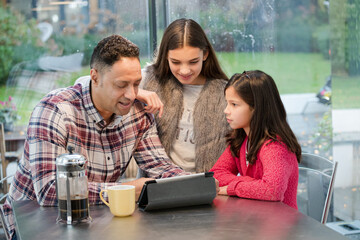 Father and daughters using digital tablet in morning kitchen