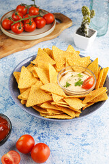 A blue bowl with cheese tortilla chips and a chilli cheese dip on a blue marble surface