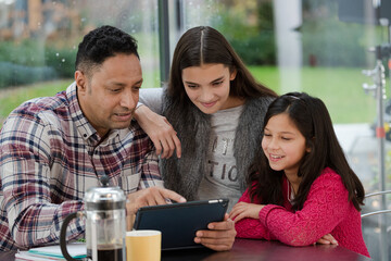 Father and daughters using digital tablet in morning kitchen