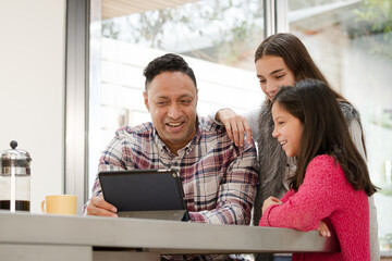 Father and daughters using digital tablet in morning kitchen