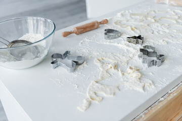 glass bowl, sieve, cookie cutters and rolling pin on white table with scattered flour