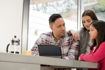 Father and daughters using digital tablet in morning kitchen