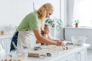 woman with daughter cooking in kitchen near table with raw dough and cooking utensils