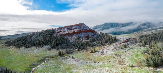 Aerial panorama of pristine snowy valley in the morning with red rock bluff jutting into the blue...