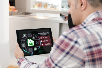 Obraz premium Man setting smart home alarm system from digital tablet on living room sofa