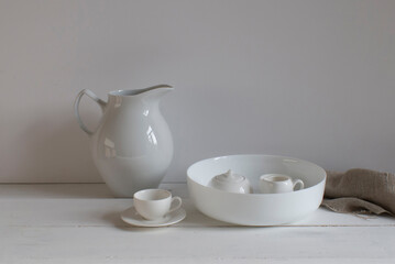 A set of white porcelain dishes on a wooden plank table, linen fabric against a light wall background.
