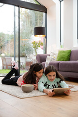 Sisters using digital tablet on living room floor