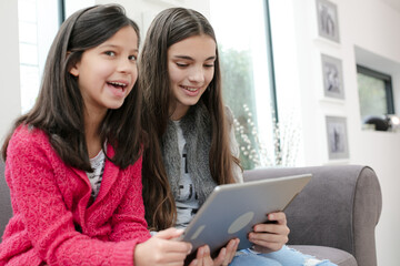 Happy sisters using digital tablet on living room sofa