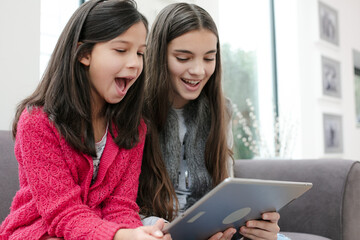 Happy sisters using digital tablet on living room sofa