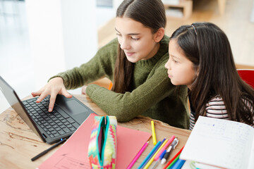 Girl helping young sister with homework on laptop