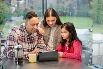 Father and daughters using digital tablet in morning kitchen