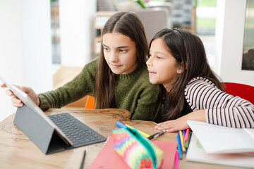 Sisters doing homework, sharing digital tablet at table