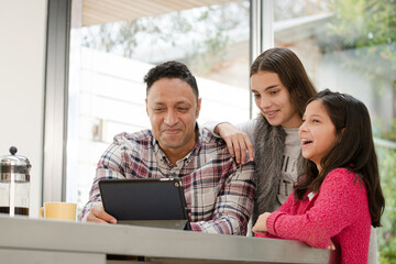 Father and daughters using digital tablet in morning kitchen