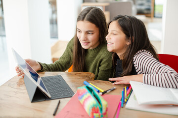 Sisters doing homework, sharing digital tablet at table