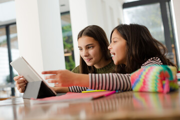 Sisters doing homework, sharing digital tablet at table