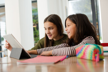 Sisters doing homework, sharing digital tablet at table