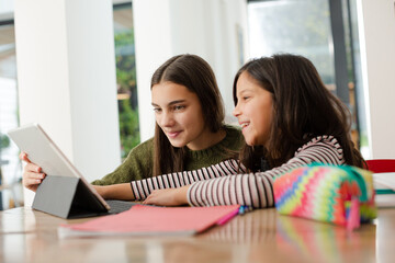 Sisters doing homework, sharing digital tablet at table