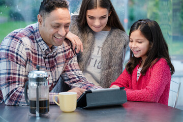 Father and daughters using digital tablet in morning kitchen