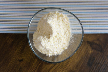Glass bowl of wheat flour on wooden kitchen table, top view.