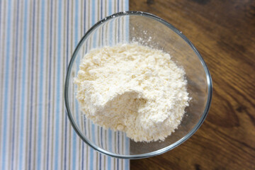 Glass bowl of wheat flour on wooden kitchen table, top view.