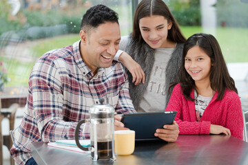 Father and daughters using digital tablet in morning kitchen