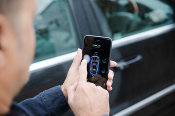 Man setting car alarm from smart phone in driveway