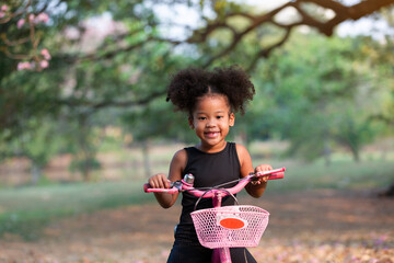 African American little curly cute girl riding bicycle in the park. Kid playing with bicycle in garden