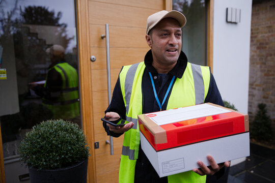 Portrait Confident, Friendly Deliveryman With Package And Smart Phone At Front Door