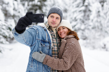 Obraz premium happy couple hugging and taking selfie photo in winter forest