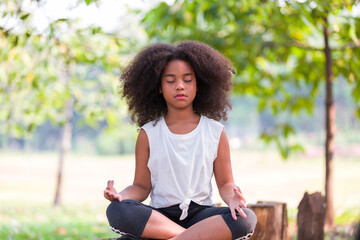 African American little girl doing meditate yoga asana with eyes closed outdoor in park. Kids girl...
