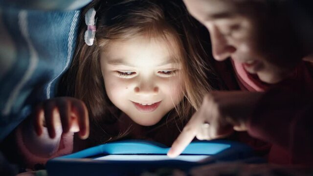 happy mother and daughter using tablet computer under blanket playing games on touchscreen technology relaxing having fun before bedtime 