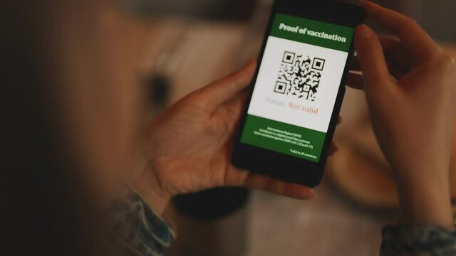 Woman checking smartphone app with certificate of immunization in restaurant. Status is invalid.