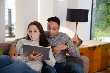 Couple relaxing, using digital tablet on living room sofa