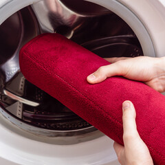 Man or woman washes red bath mat. Washing carpet in washing machine