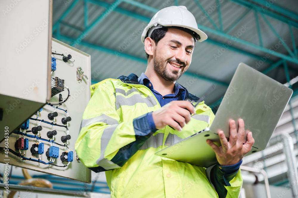 Wall mural young male machine inspector wearing vest and hardhat with headphones checking machine and sterilize