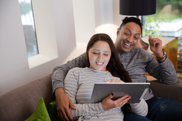 Couple relaxing, using digital tablet on living room sofa
