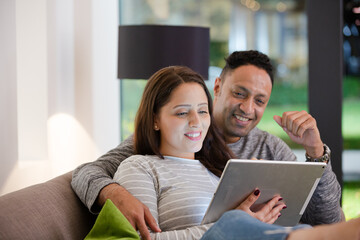 Couple relaxing, using digital tablet on living room sofa