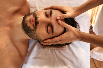 Relaxing anti-stress head massage. Handsome man relaxes in a massage parlor during head massage, top view