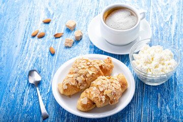 Breakfast, fresh French croissant with a cup of coffee and cottage cheese on a blue wooden table.