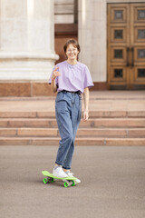 brunette teen girl with glasses with a green skateboard on the streets of the city on a clear sunny day