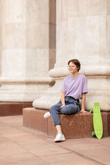 brunette teen girl with glasses with a green skateboard on the streets of the city on a clear sunny day