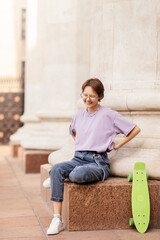 brunette teen girl with glasses with a green skateboard on the streets of the city on a clear sunny day