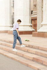 brunette teen girl with glasses with a green skateboard on the streets of the city on a clear sunny day