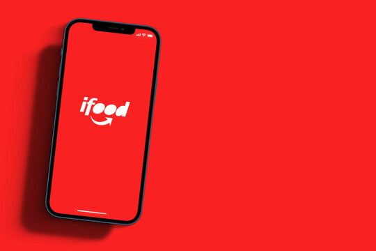Ifood app on smartphone screen with large shadow marked giving the feeling that you are taller on red background. Rio de Janeiro, RJ, Brazil. September 2021.
